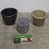 Overview photo showing two planter pots (one dark brown with honeycomb pattern and one beige with bamboo design), galvanized tin bucket, and green boxed garden tool set