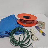 Overall view of blue tarp, orange extension cord reel with orange cord, twine, utility line cord, green and white extension cords.