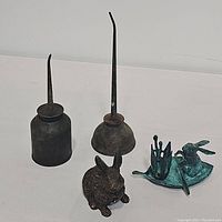 Four vintage metal items shown on a white surface: two oil cans, one metal rabbit, one brass bunny on leaf raft candle holder.