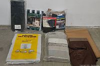 Assortment of seven patio furniture covers in various colors and packaging, including a yellow vinyl cover, white cover, brown cover, black cover, grey cover in plastic, and beige cover.