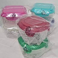 Photo showing several round plastic containers with colored lids including pink, turquoise blue, red, and green, each wrapped in clear plastic bags indicating they are new.