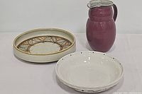 Frank view of the three serving items: round serving bowl with leaf design, white pie plate, and red jug.