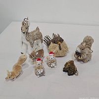 Photo showing 8 assorted straw animal figurines grouped on flat white surface. Deer, bird, squirrel, owls, hedgehog and small rodents visible.