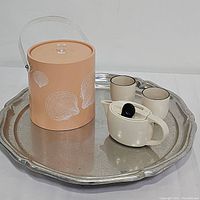 Photo showing peach vinyl ice bucket with sea shell design, two ceramic tea cups, cream tea pot with black lid and large pewter tray underneath