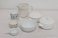 Photo showing all white ceramic serving pieces including the measuring jug with volume markings, lidded casseroles, round bowl, lotus dishes, soup bowl, and side bowls.