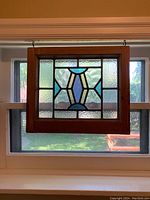 Full view of antique stained glass panel hanging in front of window, showing entire wood frame and glass design.