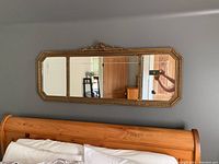 Wall-mounted antique rectangular mirror above bed with ornate gold frame and decorative top crest.