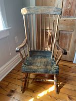 Front view of solid wood antique rocking chair showing spindle back, wide seat, and curved armrests.