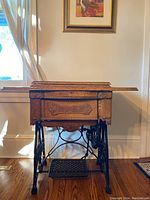 Front view of the New Home antique sewing machine cabinet with fold-over wooden top and cast iron treadle base.