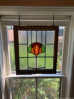 Full view of the stained glass panel hanging in a window showing the wooden frame and textured glass design.
