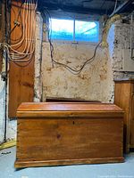 Front view of closed antique solid wood trunk, showing keyhole on front panel and natural wood finish.