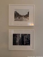 Two white-framed black and white cityscape photos hung on a wall, one showing Paris Champs-Élysées with Arc de Triomphe and the other a New York street scene.