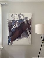 Full view of the abstract textured canvas art on a wall with lamp beside it, showing blue, brown and grey color palette.