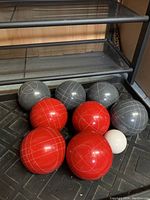 Photo of 4 red bocce balls and 4 grey bocce balls arranged together with the white pallino ball.