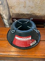 Photo of the black plastic circular Christmas tree stand showing three metal tightening screws and product label.