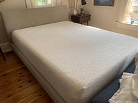 Queen size foam mattress on upholstered bed frame angled side view showing mattress and bed frame details.
