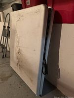 White folding table in folded position showing dirty, scuffed surface