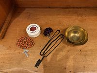 Photo showing all items including rosary, Vatican container, purple boutonniere clip, and brass holders on wooden surface