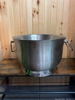 Front view of the large stainless steel ice bucket showing handles and overall shape against wooden wall background.