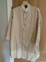 Full front view of the men's Indian kurta jacket showing intricate light gold floral pattern on cream fabric, long sleeves, collar, and button closure