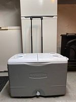 Front view of gray Rubbermaid cooler with closed lid, telescoping handle extended, white background.