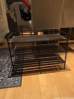 Angle view of shoe rack showing three horizontal slatted shelves in dark brown metal.