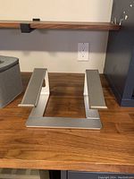 Front view of silver laptop stand placed on wooden desk under a shelf.