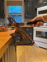Side view of bronze wine opener clamp-mounted on wooden table, wooden handle held by hand.