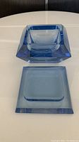 Blue glass Art Deco trinket box and lid separated, showing square shape and faceted edges in light blue glass.