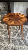 Front view of octagonal side table with geometric wood inlay pattern on top, standing on four curved legs on a carpeted floor.