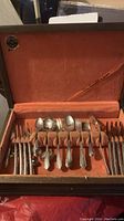 Open case showing knives, forks, spoons, and other flatware pieces arranged in orange velvet slots.