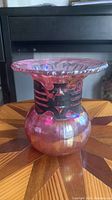 Front angle view of vintage iridescent art glass vase showing bulbous base, flared iridescent pink top, and black metal decorative collar.