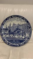 Full view of the vintage large blue Delft plate showing complete hand-painted horse carriage and buildings scene with decorative border.