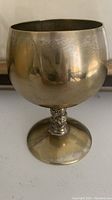 Front view of vintage silver plated goblet showing curved bowl, decorative stem and flat base with visible tarnish and reflections.