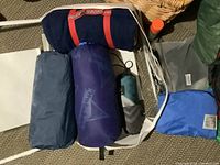 Multiple sleeping bags and camping gear arranged together showing different colors and style, focus on sleeping bags and small accessories.