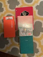 Five spiral notebooks of different sizes and cover designs placed flat on a patterned surface.