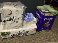Image of bulk lot including two Vanity Fair napkin packs (240 and 660 napkins), two Kleenex Ultra Soft tissue 12-pack boxes, and small Puffs tissue packs.