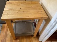 Front view of butcher block kitchen side cart showing wooden top, stainless steel shelf, towel bars and hooks on three sides.
