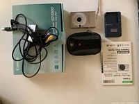 Overview photo showing all items: camera, box, charger, cables, carrying case, and user manual.