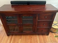 Front view of wooden sideboard showing two glass doors and three drawers with metal handles, with a soundbar placed on top.