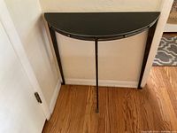 Front and right side view of the dark metal half-moon side table showing its shape and leg positioning against a wall.