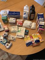 Overview of assorted first aid items arranged on a round wooden table, including boxes of cotton tipped applicators, disposable gloves, antiseptic liquids, and bandage packages.