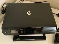 Closed HP Envy 4500 printer scanner unit showing top with HP logo and front LCD control panel and paper tray.