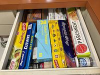 Top view of drawer showing various kitchen paper products including Glad Cling Wrap, Reynolds Wax Paper, Glad Gallon Freezer Bags, Reynolds Aluminum Foil, and Cinnamon flavor parchment paper.