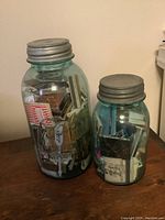 Front view of two glass jars, one large and one small, both filled with matchbooks and topped with antiqued metal lids.