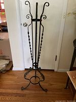 Full view of the metal plant stand showing three curved feet and two circular holders for plant pots.