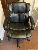 Front view showing padded black leather seat, backrest with panel stitching, and armrests.