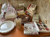 Photo showing various paper plates, plastic cups, and multiple packs of paper napkins with different patterns on a kitchen counter.