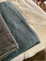 Folded gray plush blanket with stripe detail and blue plush blanket laid out on cream surface.