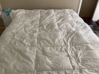 Full view of white down comforter spread on bed showing quilted square stitch pattern and overall clean surface.